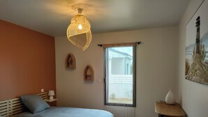 A bedroom with two beds, a hanging light fixture, a window with curtains, and a painting on the wall.