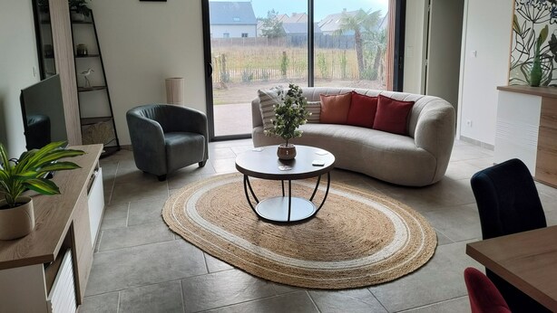 A modern living room with a sofa, armchair, and a coffee table. There is a large window providing a view of the outside.