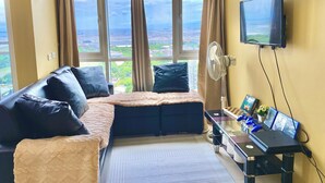 A bedroom with a large window, a bed, a desk with a laptop, and a TV. - 180° Manila View near Airport, MOA, PICC and World Trade Center w/ Massage chair (Pasay City)