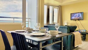A dining area with a table set for four, a sofa, and a TV mounted on the wall. - 180° Manila View near Airport, MOA, PICC and World Trade Center w/ Massage chair (Pasay City)