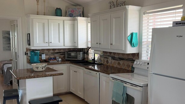 A kitchen with white cabinets, a microwave, a toaster, and a refrigerator. - Oceanfront 2 bedroom house with WiFi in Freeport on 45 acres. (Freeport)