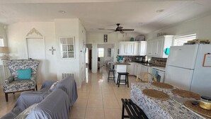 A spacious living area with a sofa, a dining table with placemats, a kitchen with white cabinets, and a ceiling fan. - Oceanfront 2 bedroom house with WiFi in Freeport on 45 acres. (Freeport)
