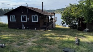 En træhytte med veranda, skorsten og udsigt over en sø.