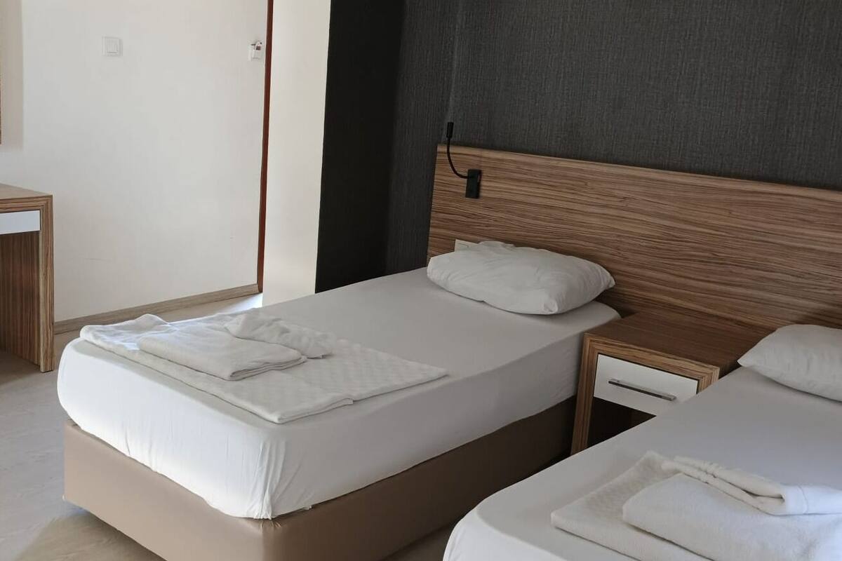 A hotel room with two beds, a wooden headboard, a nightstand, and a small desk with a chair.