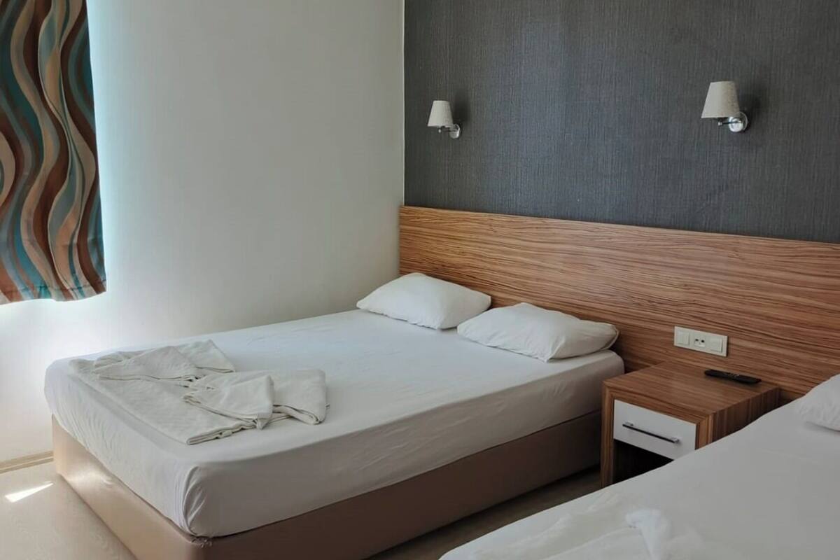 A modern hotel room with two beds, a wooden headboard, a nightstand, and a wall-mounted lamp.