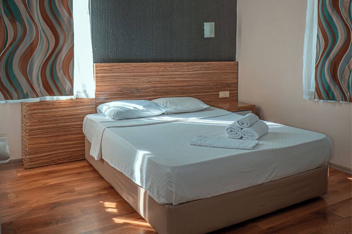 A modern bedroom with a wooden headboard, a bed with white linens, and striped curtains.