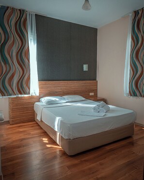 A modern bedroom with a wooden headboard, a bed with white linens, and striped curtains. - YÜCESAN SUİT HOTEL (Alanya)