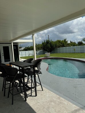 Une terrasse couverte avec une piscine, du mobilier d’extérieur et une vue sur le jardin.