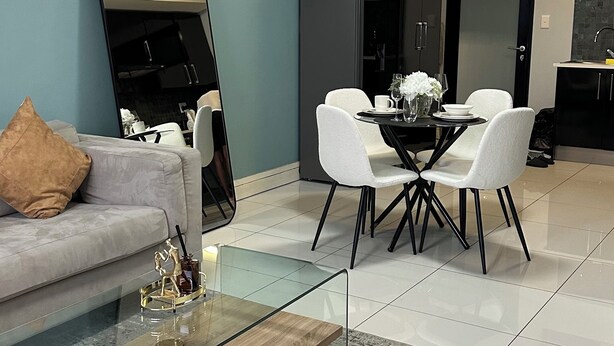 Una sala de estar moderna con una mesa de centro de vidrio, sillas blancas, un sofá y un espejo grande.