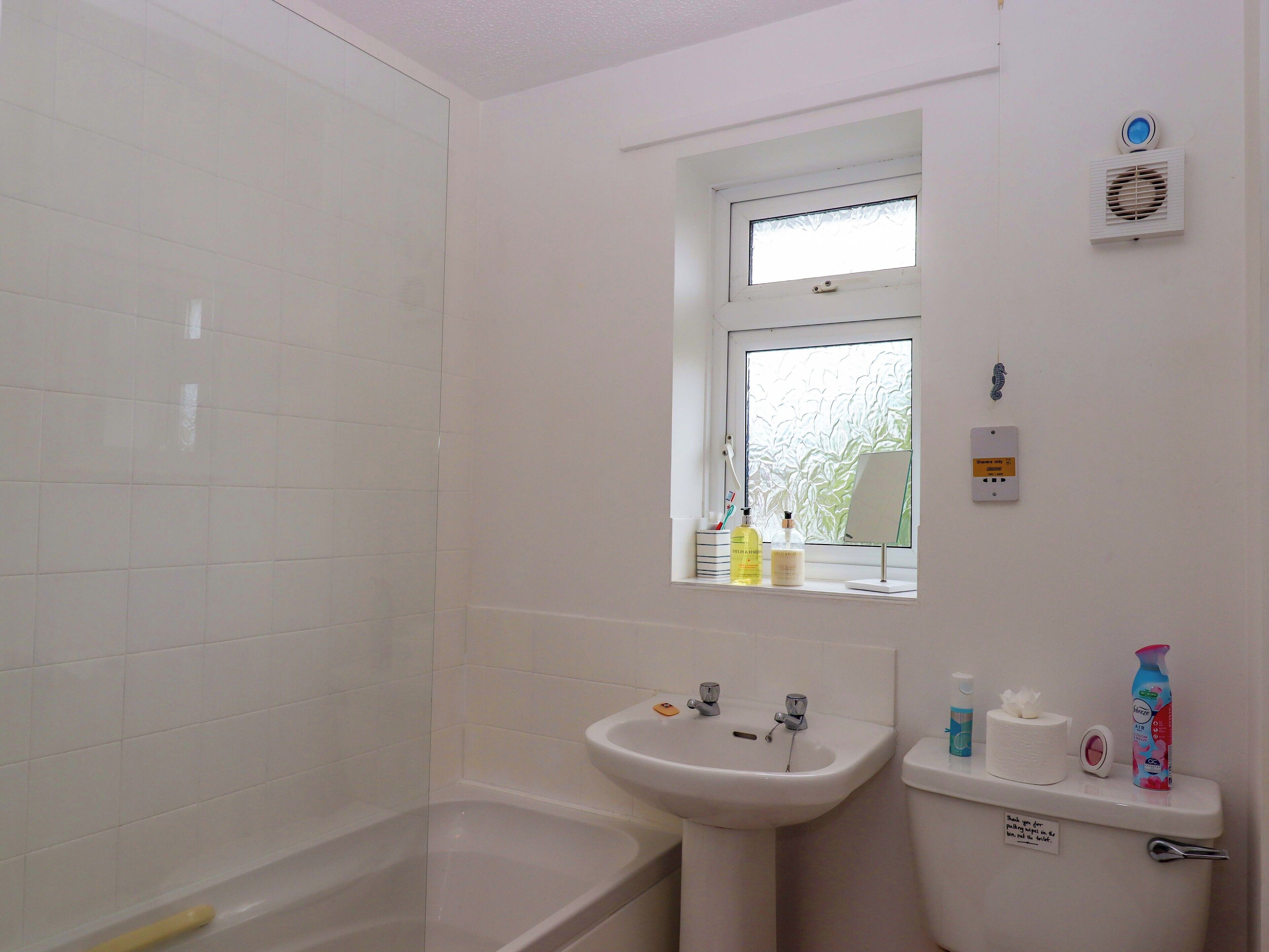 A bathroom with a bathtub, sink, and toilet. There is a window with a view of trees outside.