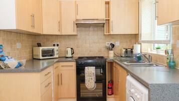 A compact kitchen with wooden cabinets, a gas stove, a microwave, a kettle, and a washing machine.