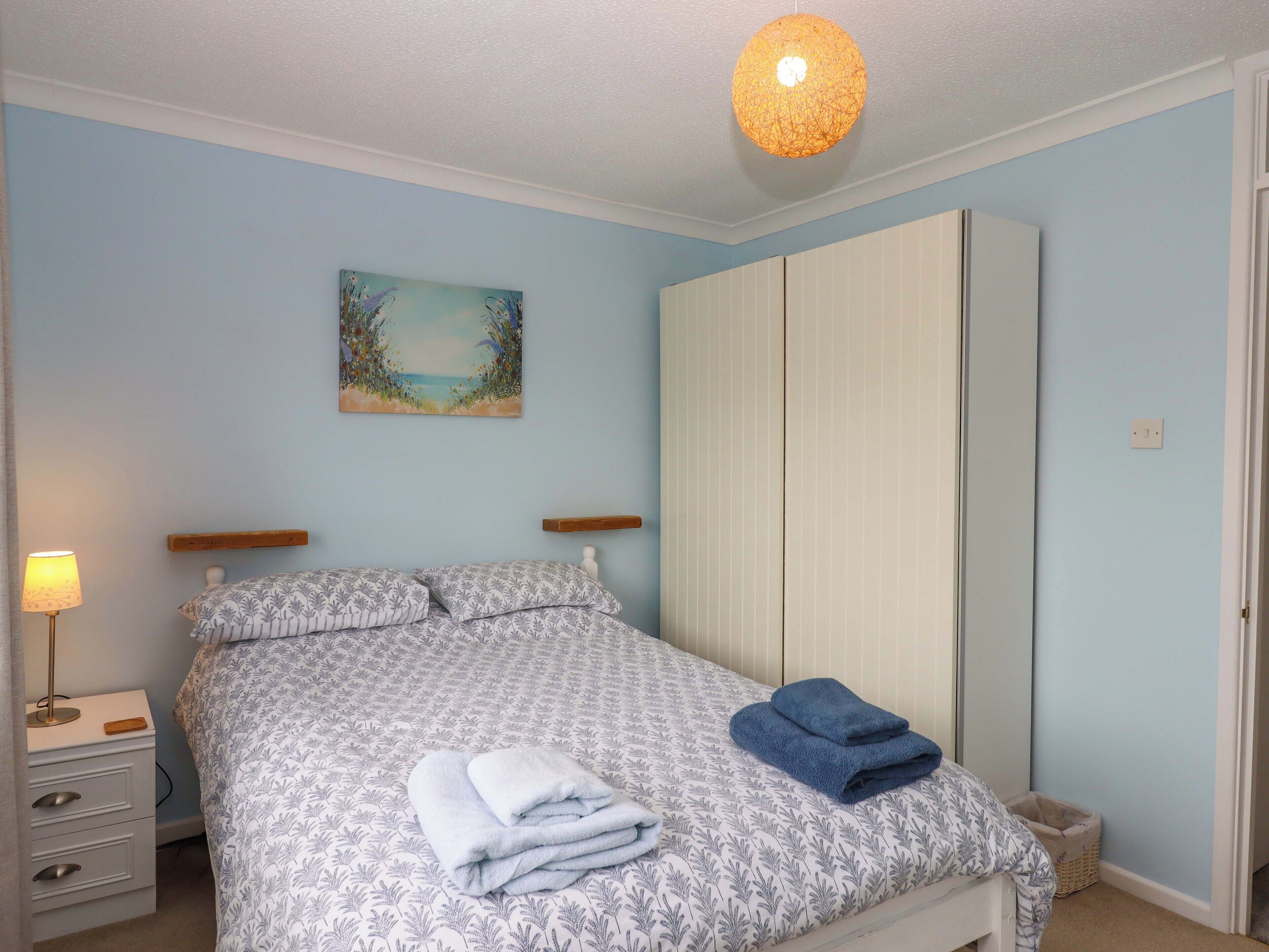 Ein Schlafzimmer mit Bett, Nachttisch, Lampe, Gemälde und Kleiderschrank.