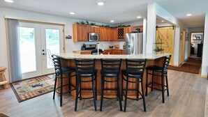 A modern kitchen with a central island, wooden cabinets, stainless steel appliances, and a bar area with stools. - Newly renovated large space - great for groups (Hayward)