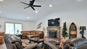 A living room with leather sofas, a stone fireplace, a television, and a ceiling fan. - Newly renovated large space - great for groups (Hayward)