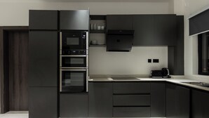 A modern kitchen with built-in appliances, a large island, and a dark color scheme. - The VVS Apartments - Two-Bedroom Apartment with Pool View (Accra)