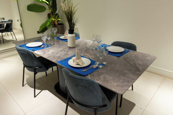 Mesa lista para comer con platos, cubiertos y copas de vino, rodeada de sillas.