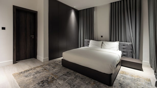 A modern bedroom with a large bed, dark wood paneling, and a grey curtain.
