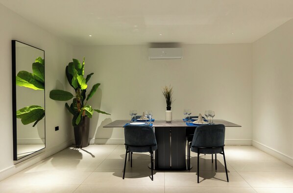 A modern dining area with a rectangular table, two chairs, and a potted plant.