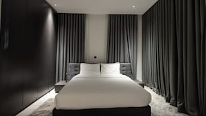 A modern bedroom with a large bed, dark walls, and heavy curtains.
