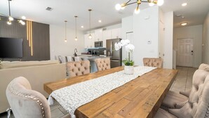 A modern dining area with a wooden table, cushioned chairs, and pendant lighting. - Beautiful 4 BR Close to Disney (Kissimmee)