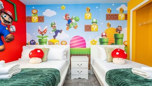 A bedroom with two beds, each with a green blanket and a pillow featuring a red mushroom. The walls are decorated with Mario and Luigi characters, and there are question blocks and coins. - Beautiful 4 BR Close to Disney (Kissimmee)
