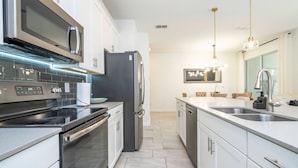 A modern kitchen with stainless steel appliances, white cabinetry, and a tiled backsplash. - Beautiful 4 BR Close to Disney (Kissimmee)
