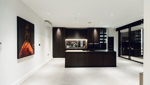A modern kitchen with a central island, dark cabinetry, and a large window providing a view of the city. - The VVS Apartments - Penthouse Apartment (Accra)