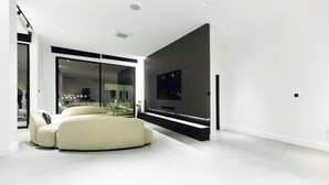 A modern living room with a large flat-screen TV, a beige sofa, and a glass door leading to a balcony. - The VVS Apartments - Penthouse Apartment (Accra)