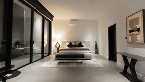 A modern bedroom with a large bed, a glass partition, and a minimalist design. - The VVS Apartments - Penthouse Apartment (Accra)