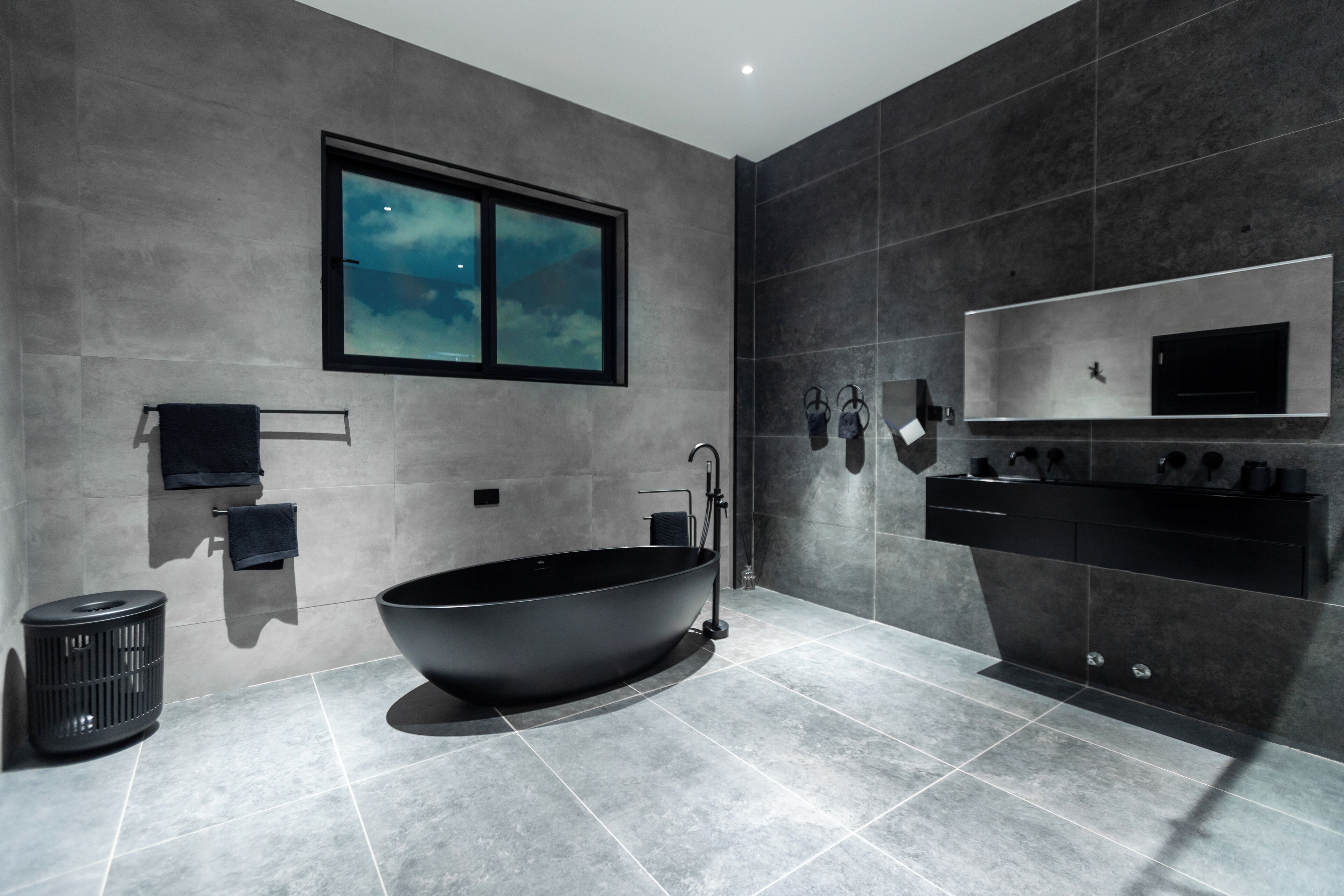 A modern bathroom with a freestanding bathtub, a large mirror, and a window with a view of the sky.
