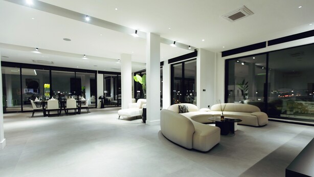 A modern living room with a sofa set, a dining area with tables and chairs, and large windows offering a city view. - The VVS Apartments - Penthouse Apartment (Accra)