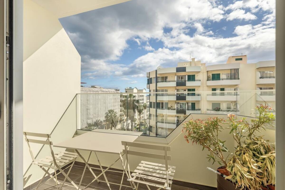 A balcony with a table and chairs, overlooking a residential area with multiple buildings and a clear sky.