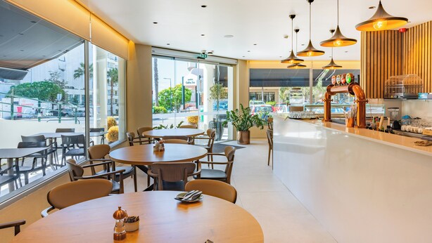 A modern cafe with round tables and chairs, large windows, and a coffee bar. - Vila Baleira Residence (Funchal)