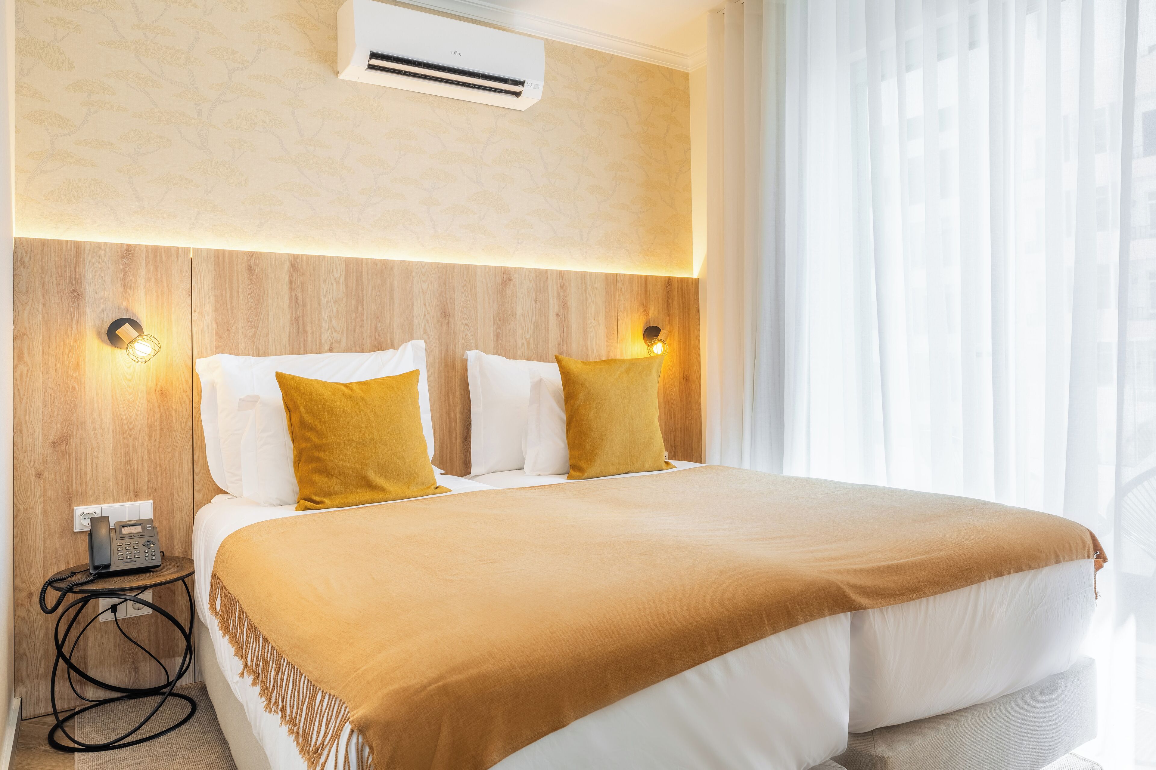 Een hotelkamer met een groot bed, twee bedlampen, een airconditioning en een telefoon op een bijzettafeltje.