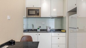 A compact kitchen with white cabinets, a microwave, a kettle, and a refrigerator. - Vila Baleira Residence (Funchal)