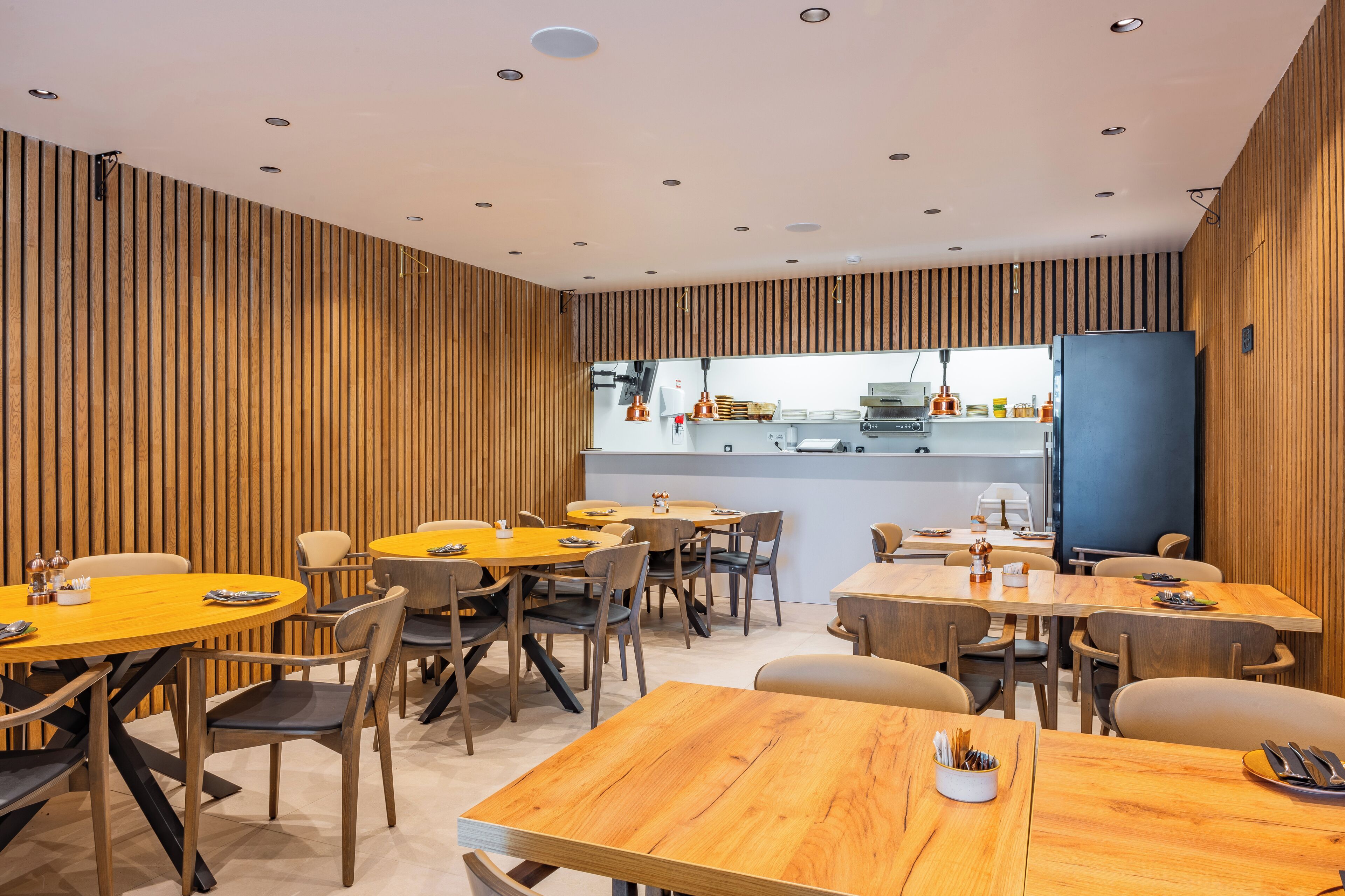 A modern dining area with wooden panel walls, multiple round tables, and chairs.
