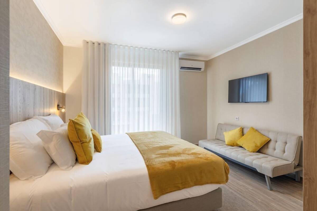 A hotel room with a bed, a sofa, a TV, and a window with curtains.