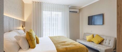 A hotel room with a bed, a sofa, a TV, and a window with curtains.