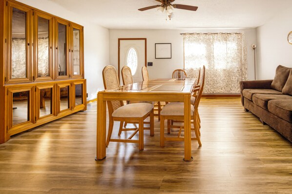 Un comedor con una mesa y sillas de madera, un aparador con puertas de cristal y un ventilador de techo.