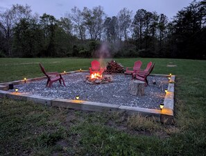 Una zona con fogata, sillas rojas y una terraza de madera.