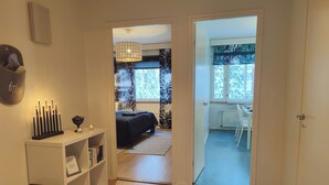 A hallway leading to a bedroom with a bed, a bedside table with a lamp, and a view of a dining area through a window. - Spacious apartment with balcony and free WiFi (Rovaniemi)