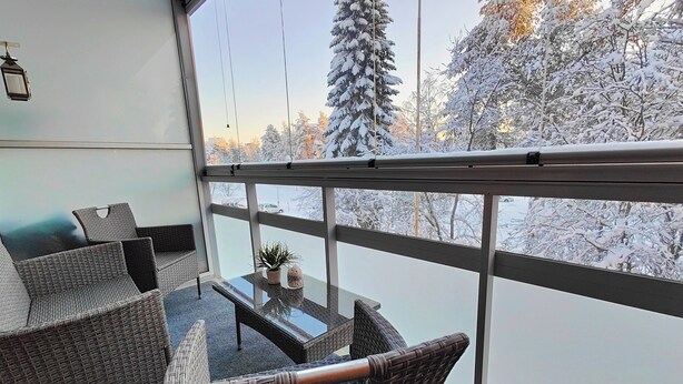 A balcony with wicker furniture and a glass table, overlooking a snowy landscape with trees. - Spacious apartment with balcony and free WiFi (Rovaniemi)