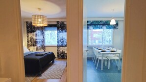A modern room with a bed, a dining area with a table and chairs, and a large window with a view of trees. - Spacious apartment with balcony and free WiFi (Rovaniemi)