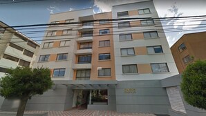 Un hotel de varios pisos con fachada moderna, entrada central y un pequeño jardín.