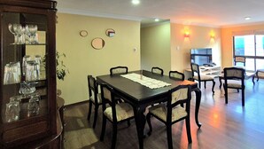 Un comedor con una mesa, sillas y un aparador con cristalería. Hay un sofá y un televisor en la sala de estar.