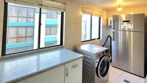 Una cocina con un refrigerador de acero inoxidable, una lavadora, un hervidor Bosch y una ventana que ofrece vistas a edificios.