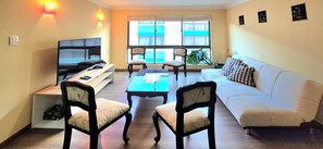 A living room with a sofa, two armchairs, a coffee table, a TV, and a window with curtains.