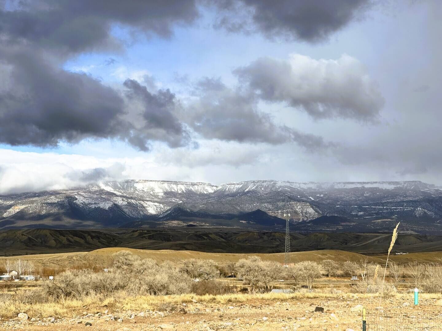 A mountainous landscape with snow-capped peaks, a clear sky, and sparse vegetation.