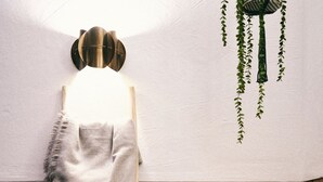 Una habitación con una escalera de madera, una pequeña mesa con velas, una silla y una planta colgante.