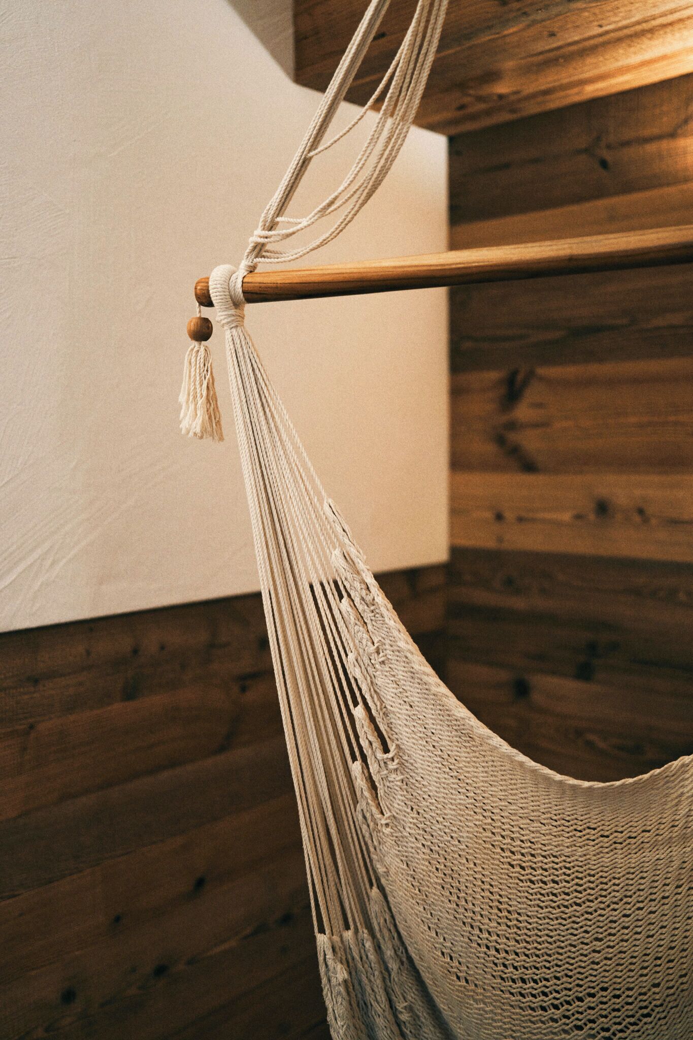 A hammock tied to a wooden beam in a room with wooden paneling.